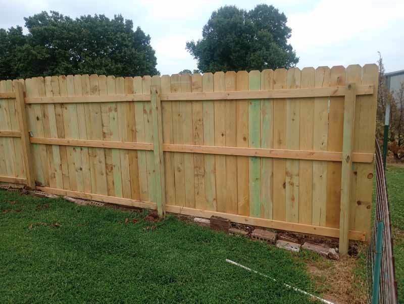 Wooden fence in a grassy yard, with a row of trees in the background.