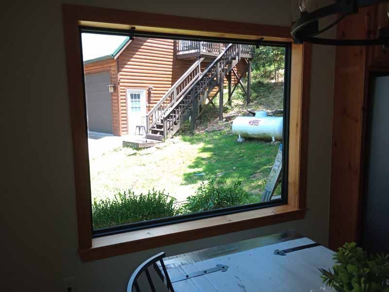 Window view of a wood-sided building with stairs and a large propane tank on a green lawn.
