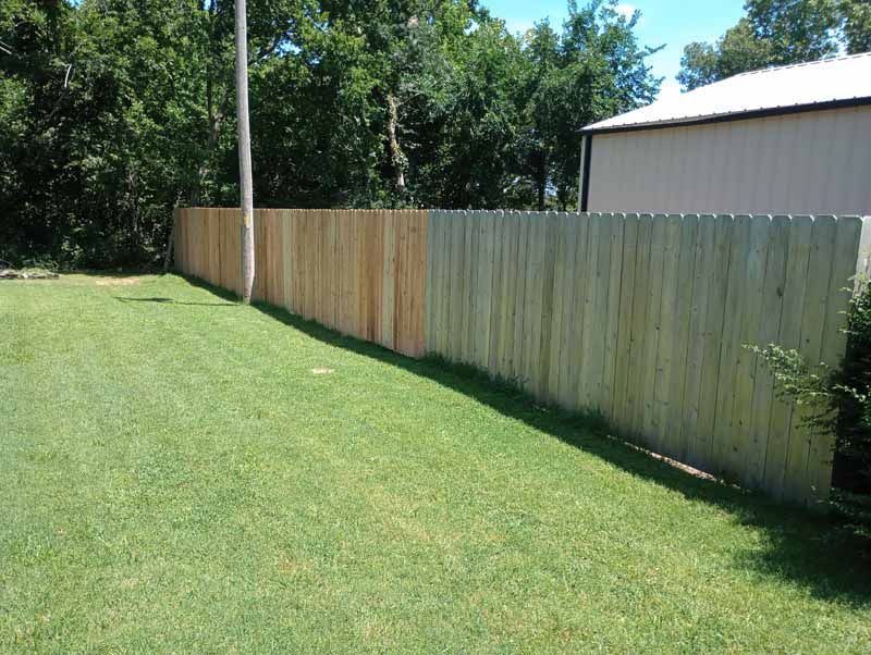 Wooden fence, half weathered and gray, half new and light brown, in green grassy yard.