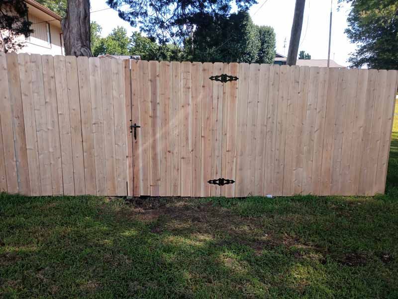 Wooden fence with gate, set in green grass. Gate has black hinges and latch.