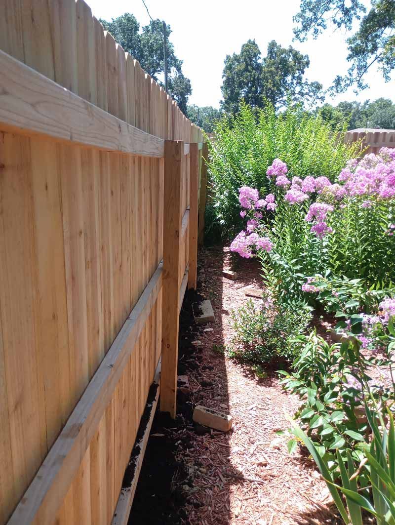 Wooden fence bordering a garden with pink flowers.