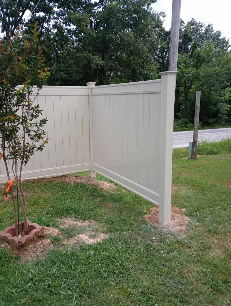 Cream-colored vinyl fence in a grassy yard, partially enclosing a small tree.