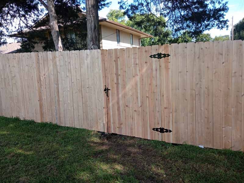 Wooden fence with gate, metal hinges and latch, grassy yard, sunny day.