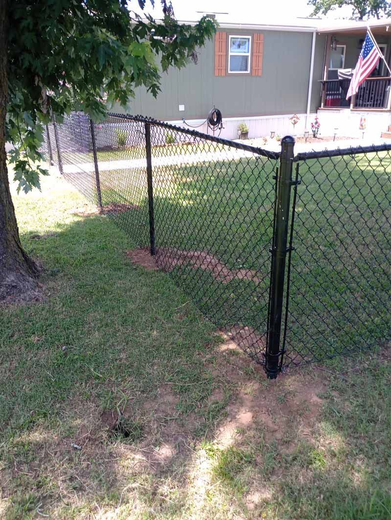 Black chain-link fence in front of a green house with an American flag.