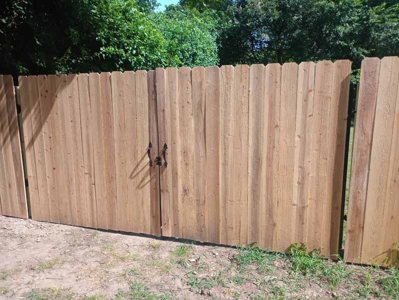 Wooden fence with a gate, in a grassy outdoor setting.