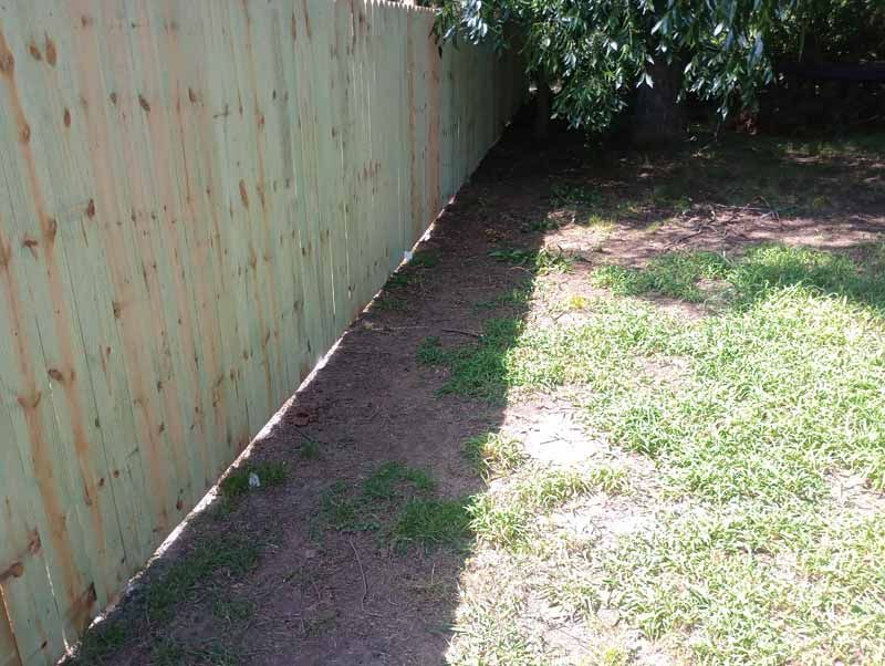 Wooden fence alongside a narrow dirt path and grass lawn.