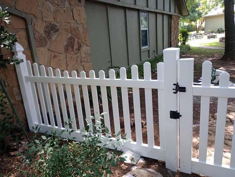 White picket fence with gate, set against a stone wall and green siding.