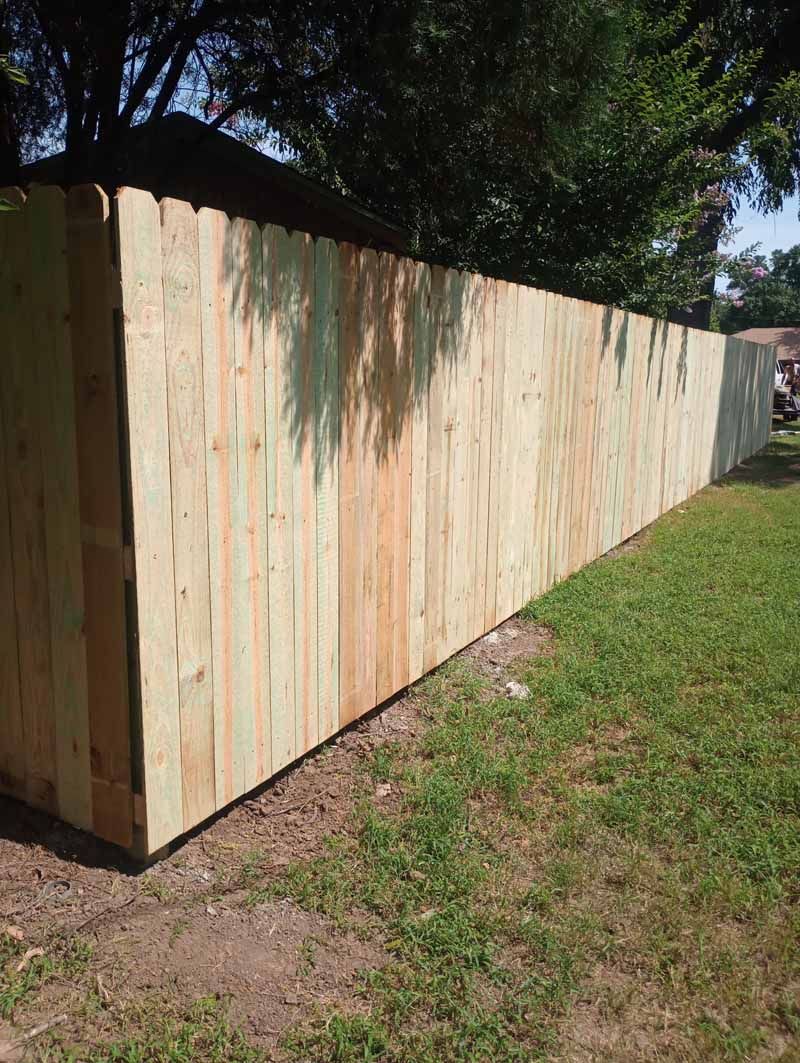 Wooden fence extending along green grass, under a blue sky.