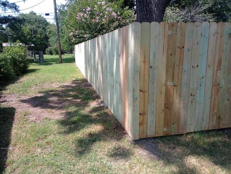 Wooden fence along a grassy yard, partially shaded.  The fence is new and the wood has varied tones.