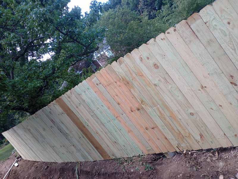 Wooden fence built on a sloped hillside next to trees.