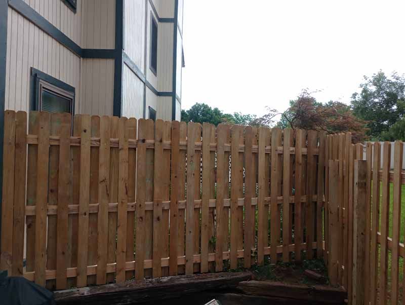 Wooden fence in front of a building, with a grassy area beyond.