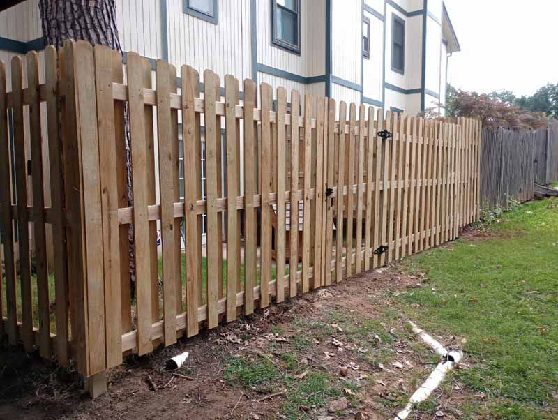 Wooden picket fence bordering a yard next to a building.