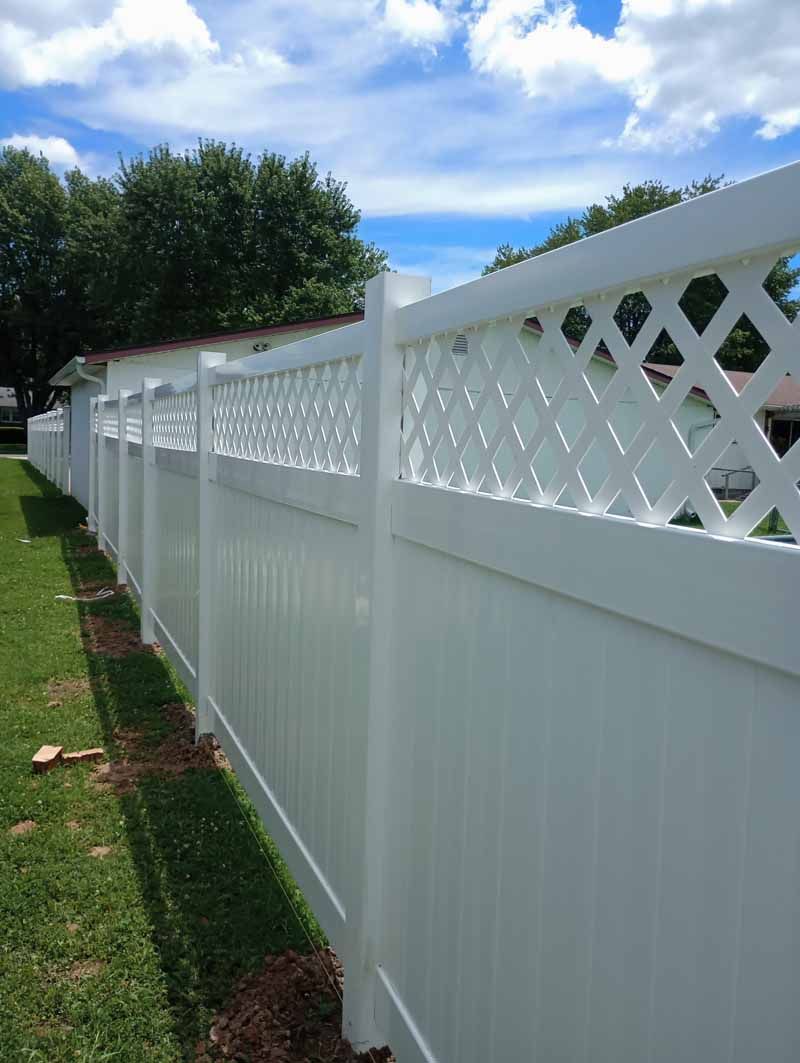 White vinyl fence with lattice top, along green grass under blue sky.