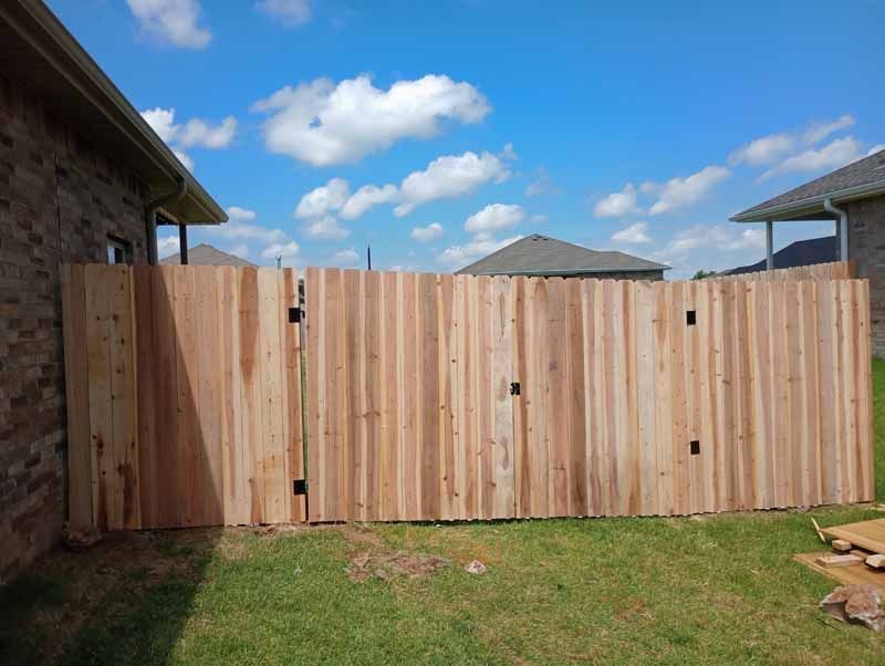Wooden privacy fence in a backyard, with a gate, against a blue sky with clouds.