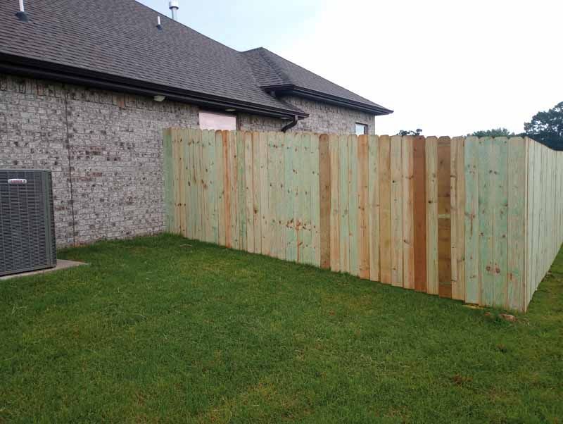 Green wooden privacy fence alongside a brick house and green lawn.