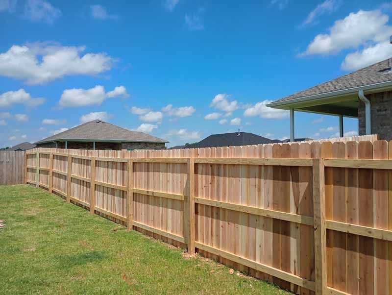 Wooden fence in a backyard, blue sky, houses in the background.