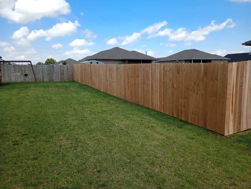 Green lawn with wood fence surrounding, blue sky with clouds in the background.