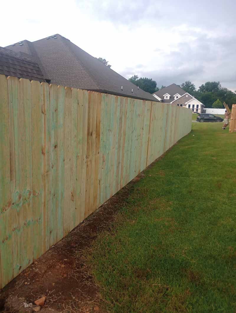 Green wooden fence along a grassy lawn, with houses visible in the background.