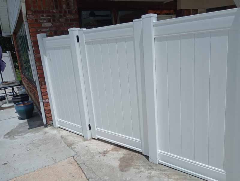 White vinyl fence sections against a brick wall and concrete ground.