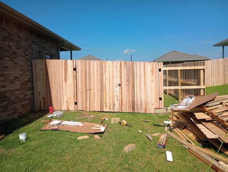 Wooden fence construction in progress on a grassy lawn with a blue sky.