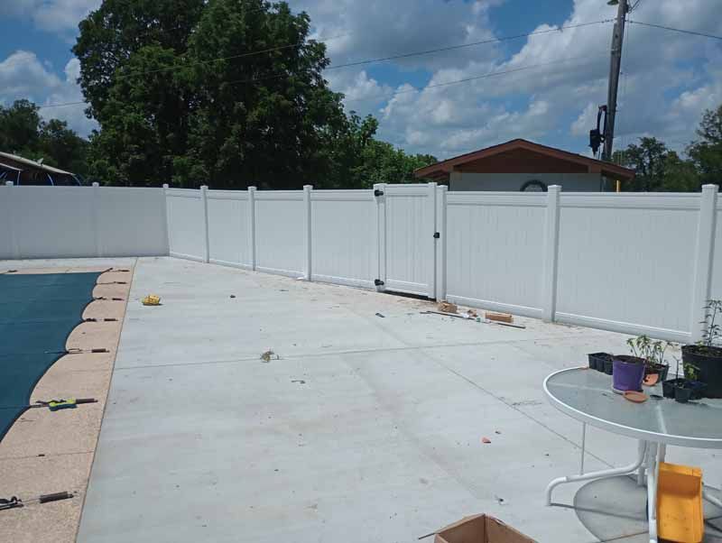 White vinyl fence enclosing a backyard with a pool, concrete patio, and a table.