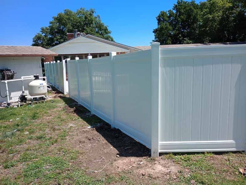 White vinyl fence in a backyard near a house and pool equipment on a sunny day.