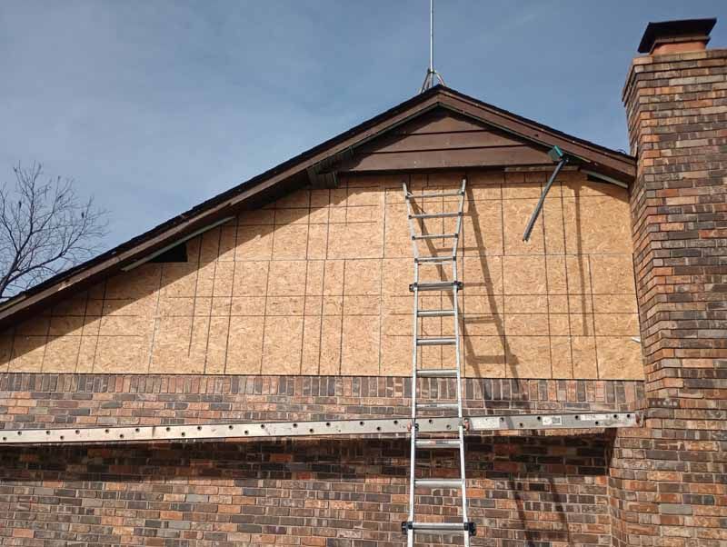 Ladder on brick building with exposed wood siding and chimney.