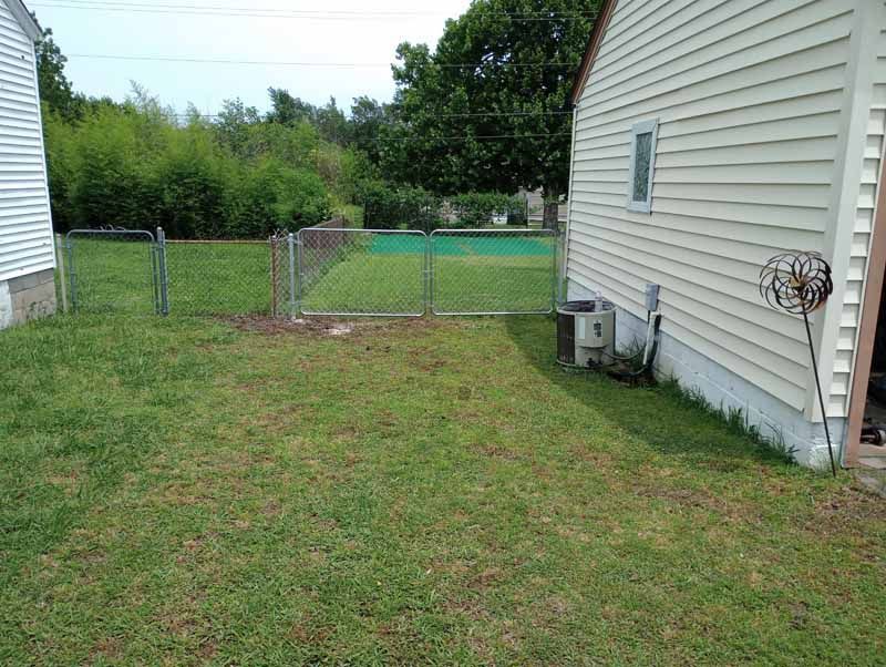 Chain-link fenced yard with green grass, small side yard between two houses.