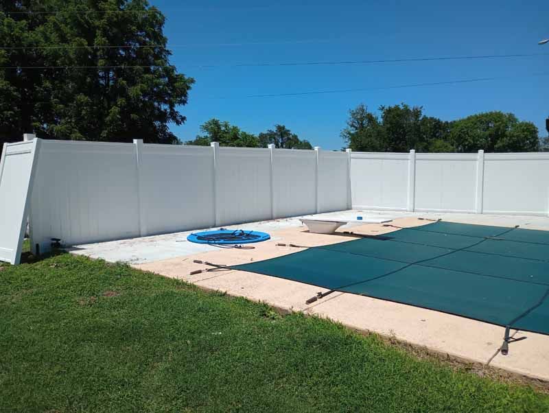 White vinyl fence surrounds a pool with a green cover on a sunny day.