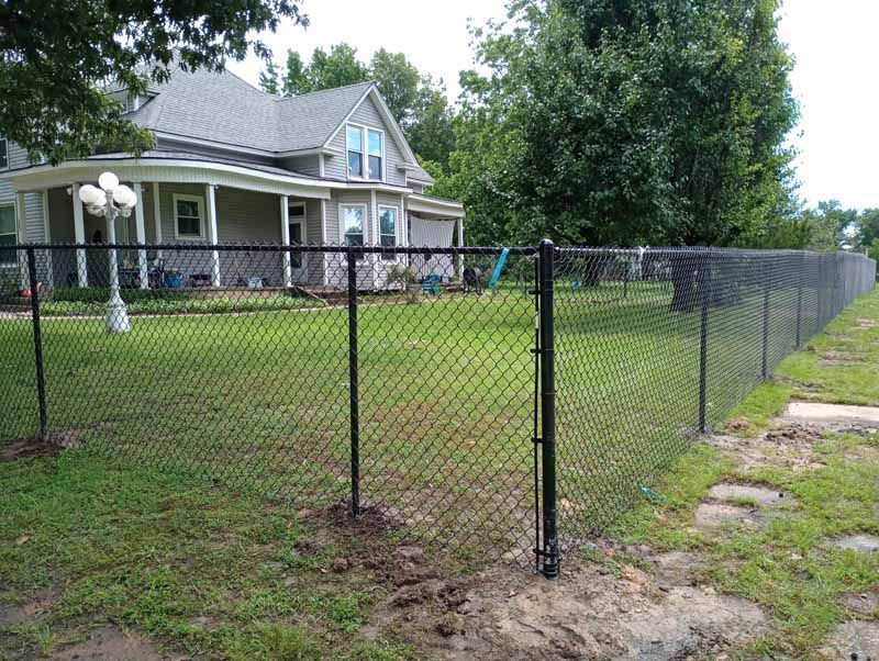 Black chain-link fence surrounds a grassy yard in front of a gray house. Gate is open.