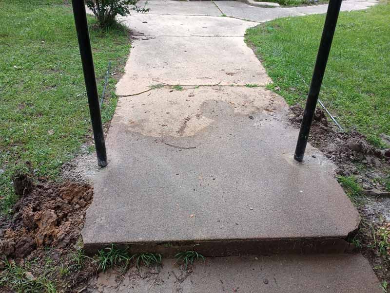 Concrete walkway with steps, flanked by grass and black support poles.