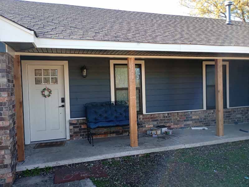 Exterior view of a house with a blue facade, a white door, and a porch with a bench.