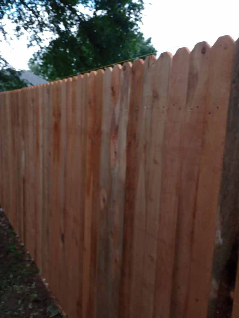 Wooden privacy fence with scalloped top, viewed at an angle outdoors.