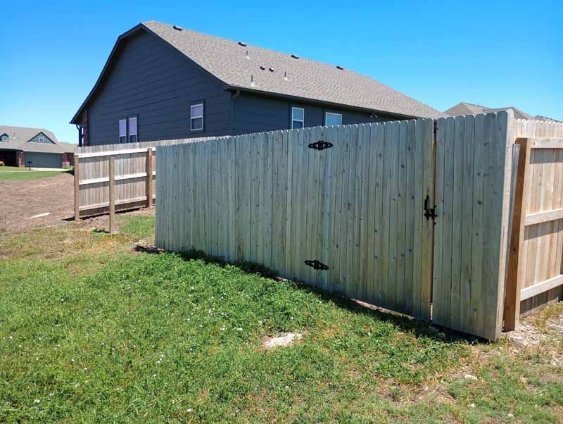 Wooden fence with gate in front of a gray house on a sunny day.