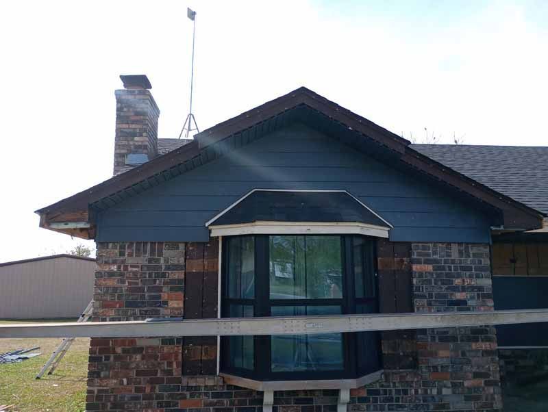 House with brick facade, blue siding, bay window, brown trim, and chimney against a sunny sky.