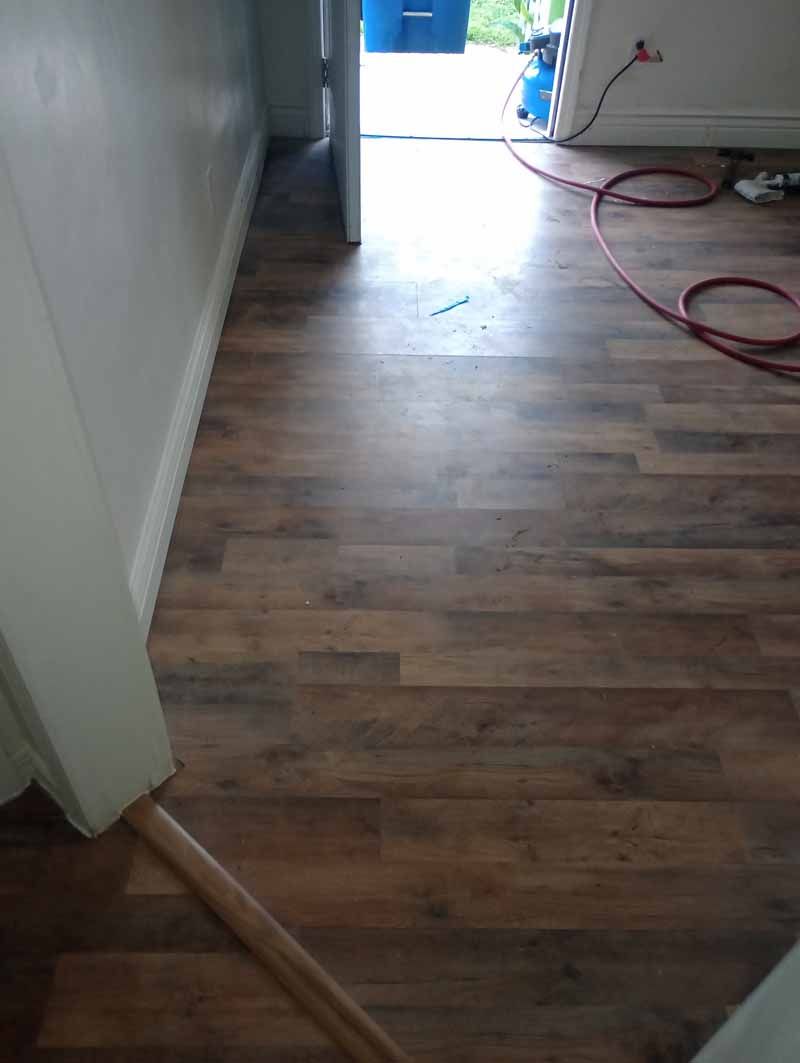 Brown laminate flooring installed in a room, doorway and white trim visible.