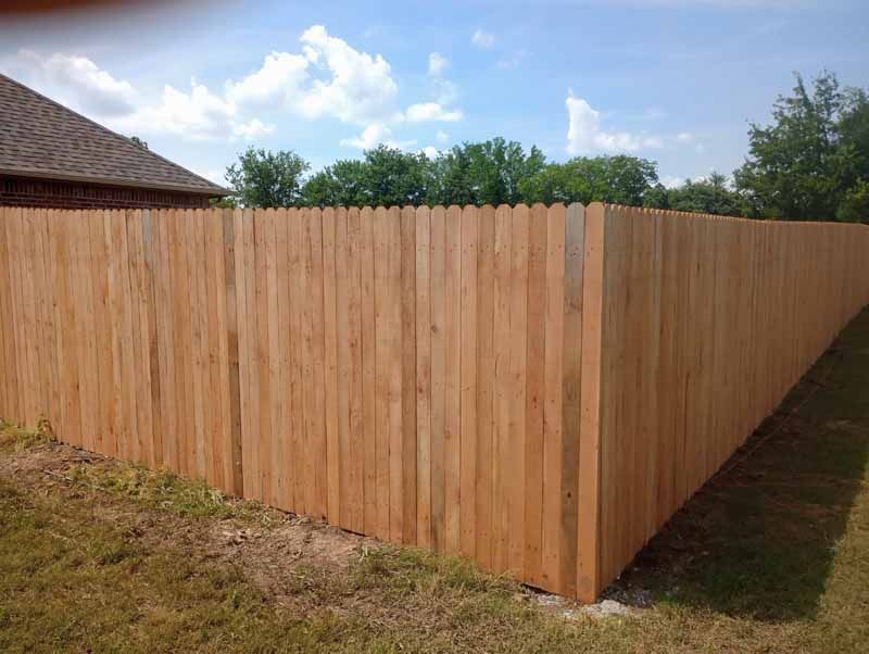 Wooden fence around a yard with a clear sky and green grass.