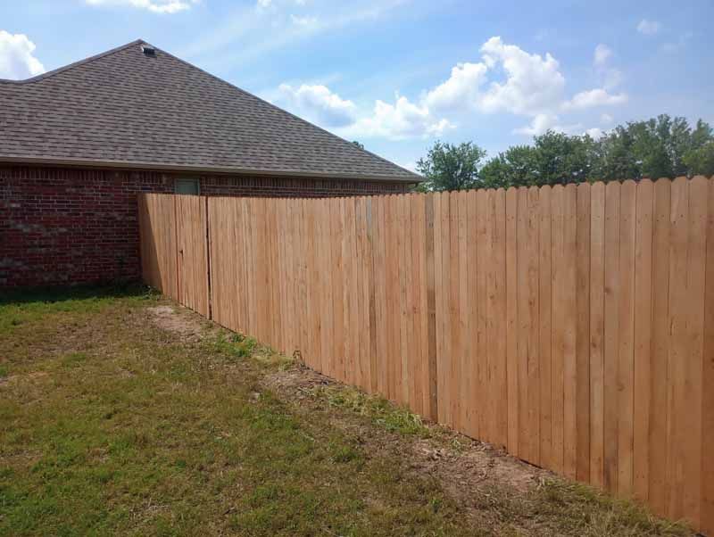 Wooden fence alongside a red brick house with green grass and a blue sky.