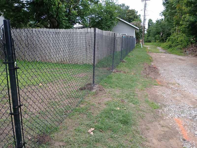Black chain-link fence bordering a grassy area and gravel path, with a building in the background.