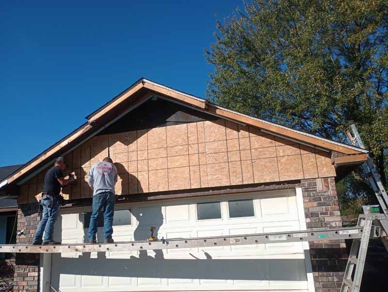Two workers installing siding on a garage under a clear blue sky.