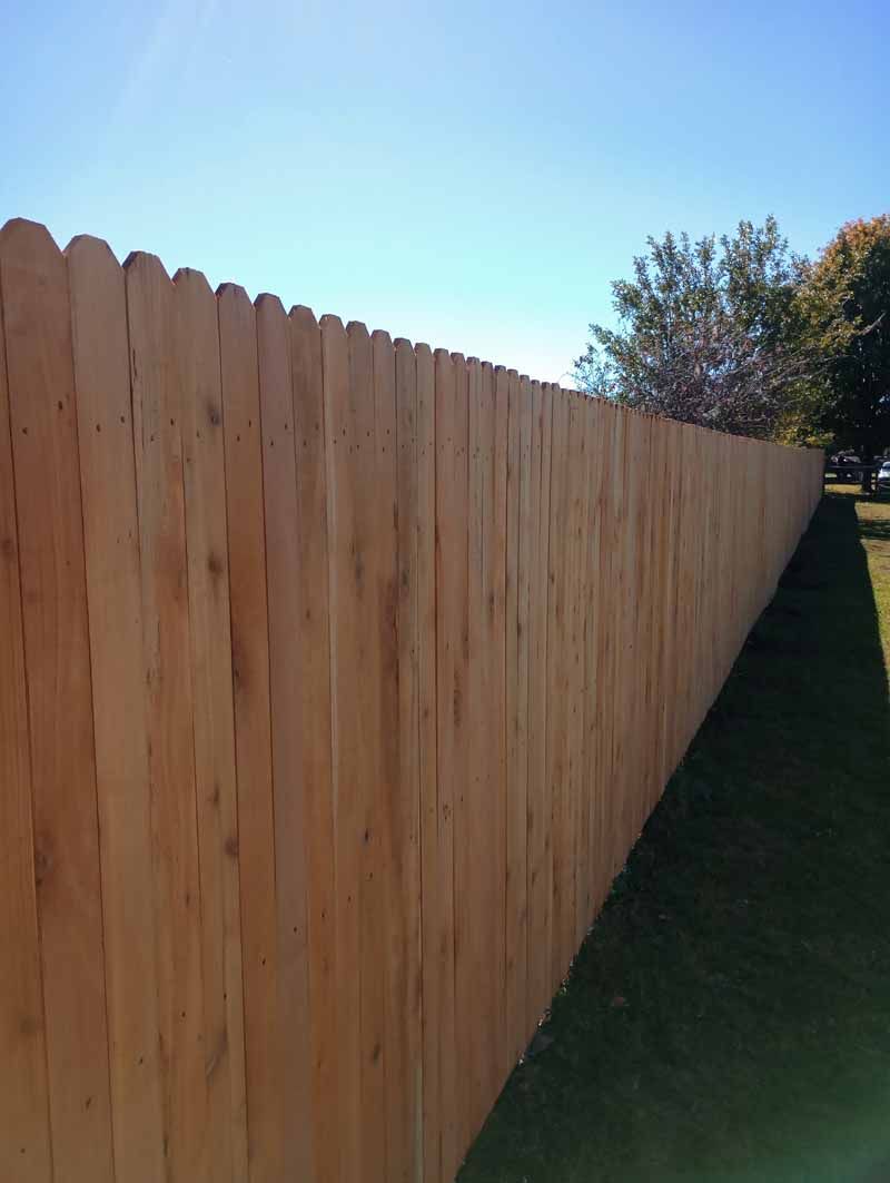 Wooden fence along a grassy lawn under a clear, blue sky.