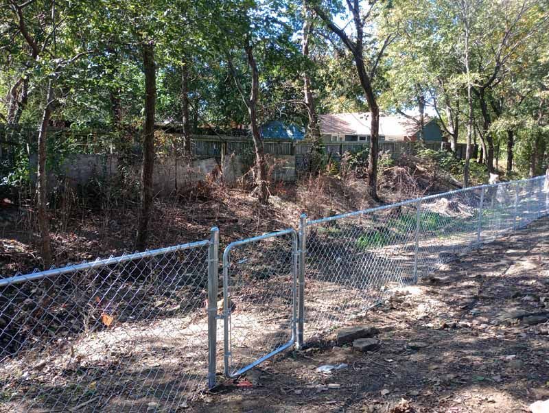 Chain link fence with gate, trees in background, and a glimpse of a house.