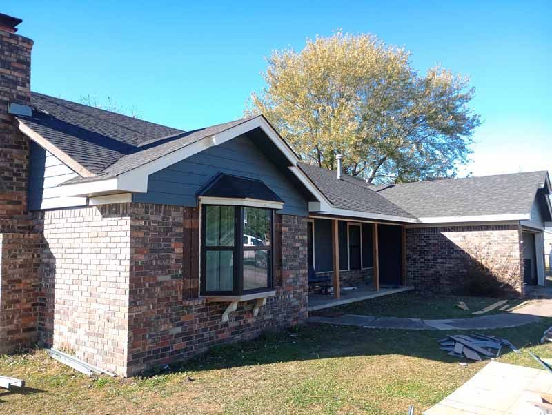 Brick house with dark blue siding, bay window, porch, and a brick chimney under a clear, blue sky.