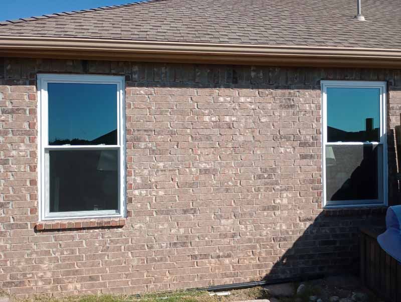 Two windows on a brick wall reflect the sky.