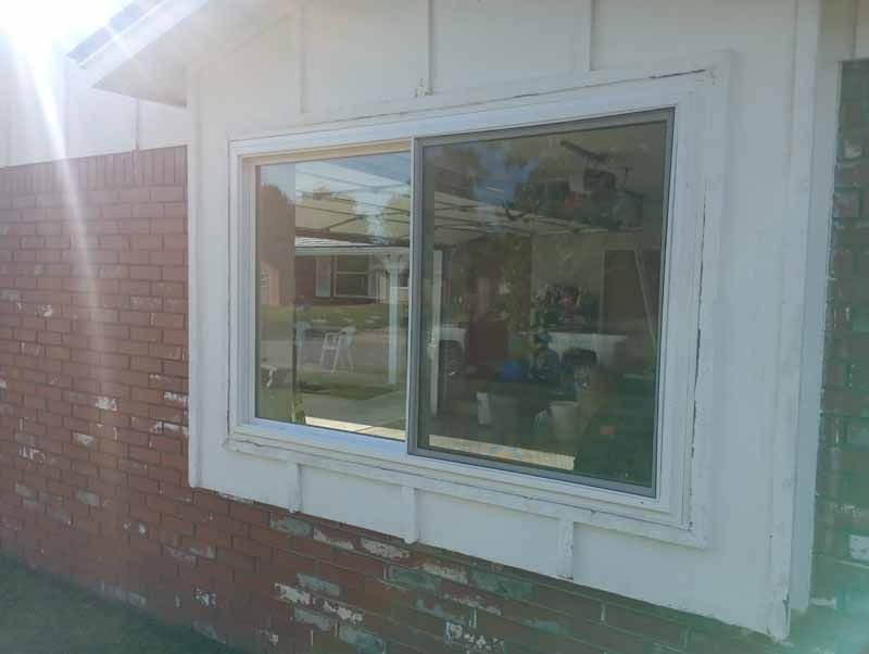 White-framed sliding window on a brick and white siding exterior. Sunlight flares from the left.