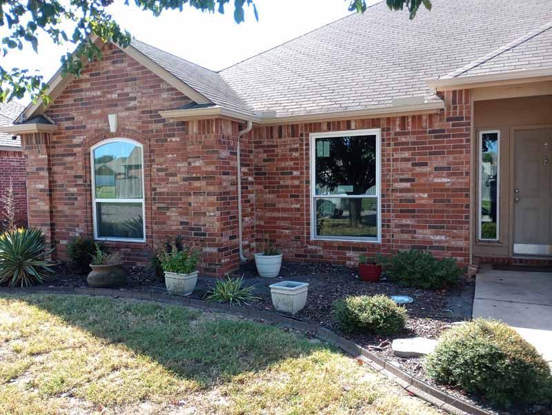 Brick house exterior with two windows, a door, and landscaping, in sunny conditions.