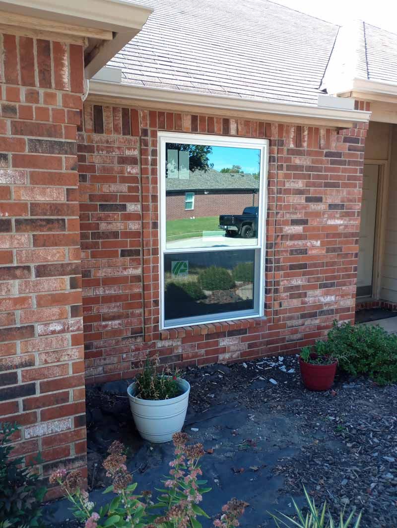 Window on a brick house reflects a yard with a black truck and landscaping.