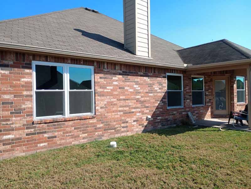 Red brick house exterior with several windows, chimney, and brown roof under a clear blue sky.