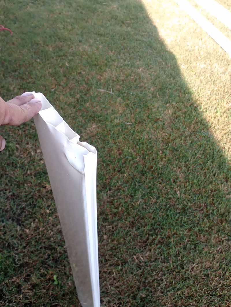 A person holds a damaged white object outdoors in front of grass.