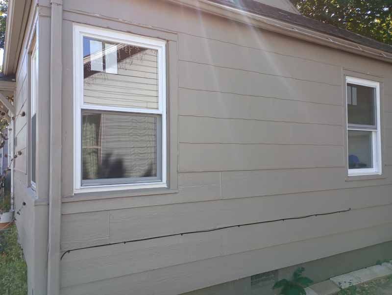 Beige house exterior with white-framed windows; sunlight shines down.